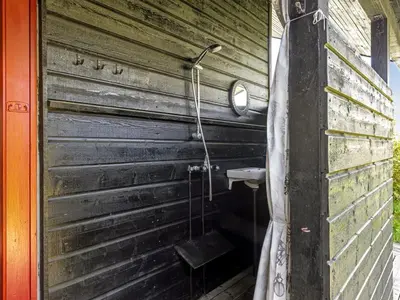 a bathroom with a wooden wall with a shower curtain at Holiday Home Gullborg - 800m from the sea by Interhome in Løkken