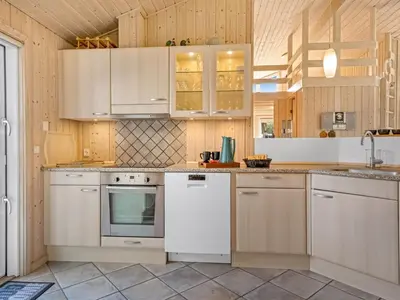 a kitchen with white appliances and wooden cabinets at Holiday Home Terho - 1km from the sea by Interhome in Løkken