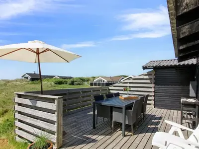 a deck with an umbrella and a table and chairs at Holiday Home Tulir - 300m from the sea by Interhome in Løkken