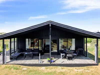 a black house with a deck with chairs and tables at Holiday Home Tulir - 300m from the sea by Interhome in Løkken