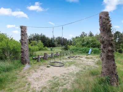 a swing set in a field between two trees at Holiday Home Siljana - 1km from the sea by Interhome in Løkken