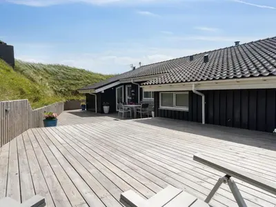 a wooden deck with a table and a house at Holiday Home Alyssa - 300m from the sea by Interhome in Løkken