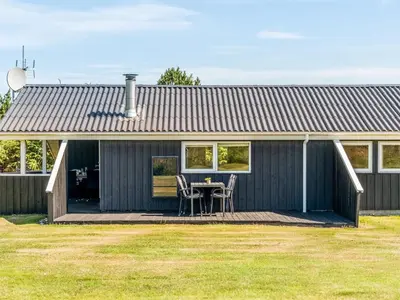 a black house with a table and chairs on a deck at Holiday Home Guja - 1km from the sea by Interhome in Løkken