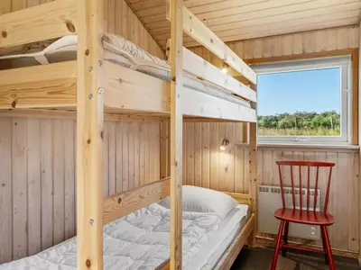 a bunk bed in a tiny house with a red chair at Holiday Home Guja - 1km from the sea by Interhome in Løkken