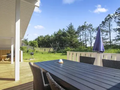 a wooden table with chairs and an umbrella on a deck at Holiday Home Eden - 800m from the sea by Interhome in Løkken