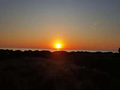 a sunset over a field with the sun setting over the ocean at Holiday Home Lauri - 350m from the sea by Interhome in Løkken