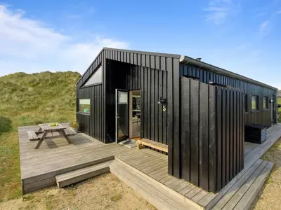 a black house with a wooden deck and a picnic table at Holiday Home Mikkel - 300m from the sea by Interhome in Løkken