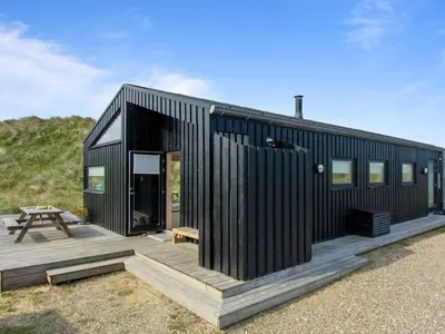 a black house with a wooden deck and a picnic table at Holiday Home Mikkel - 300m from the sea by Interhome in Løkken