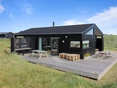 a black house with a deck in a field at Holiday Home Mikkel - 300m from the sea by Interhome in Løkken