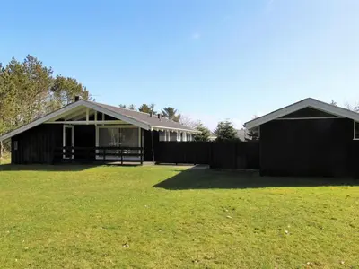 a black house with a grass field in front of it at Holiday Home Conradine - 500m from the sea by Interhome in Løkken