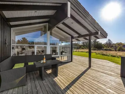 an outdoor deck with a black couch and a table at Holiday Home Asol - 650m from the sea by Interhome in Løkken