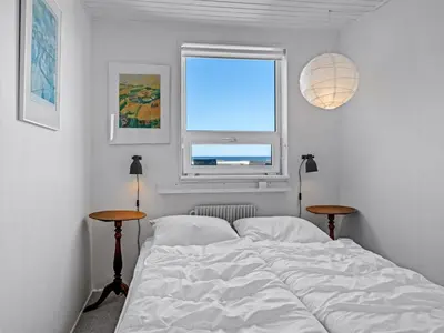 a bed in a bedroom with a window and two tables at Holiday Home Mielikki - 200m from the sea by Interhome in Løkken