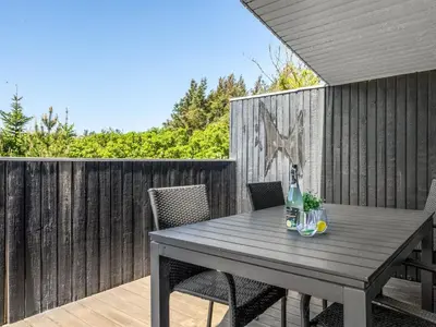 a wooden table with two chairs and a bottle on a patio at Holiday Home Tonja - 300m from the sea by Interhome in Løkken