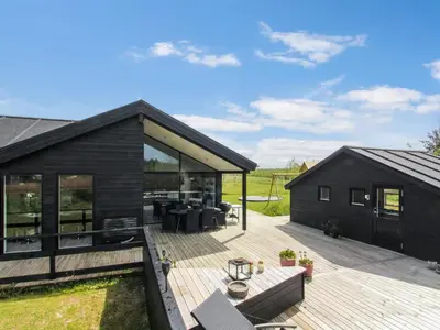 a black house with a wooden deck and glass walls at Holiday Home Aldina - 1-5km from the sea by Interhome in Løkken