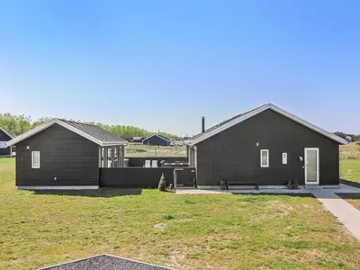 a black house with a yard with a grass field at Holiday Home Eveline - 1-5km from the sea by Interhome in Løkken