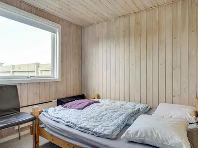 a bed in a room with a chair and a window at Holiday Home Marino - 480m from the sea by Interhome in Løkken