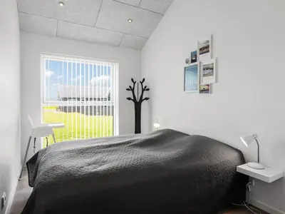 a bedroom with a black bed and a window at Holiday Home Dwerg - 1-5km from the sea by Interhome in Løkken