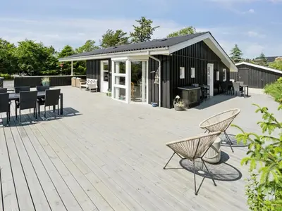 a deck with chairs and tables and a building at Holiday Home Marli - 700m from the sea by Interhome in Blokhus
