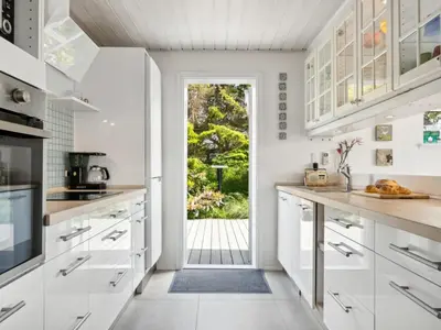 a kitchen with white cabinets and a door leading to a yard at Holiday Home Marli - 700m from the sea by Interhome in Blokhus