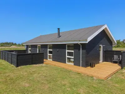 a black house with a deck in a field at Holiday Home Elenore - 900m from the sea by Interhome in Løkken