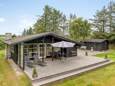 a house with a deck and an umbrella at Holiday Home Bernadeta - 1-2km from the sea by Interhome in Blokhus