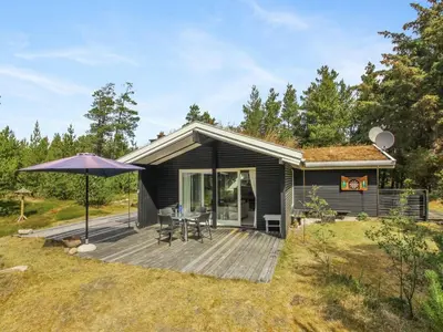 a small house with a deck and an umbrella at Holiday Home Heike - 1-3km from the sea by Interhome in Blokhus