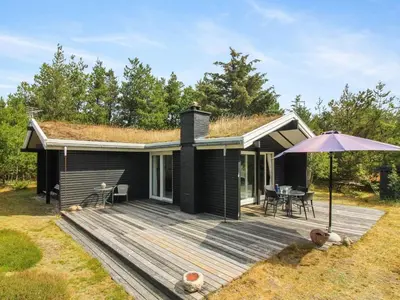 a black house with a wooden deck with an umbrella at Holiday Home Heike - 1-3km from the sea by Interhome in Blokhus