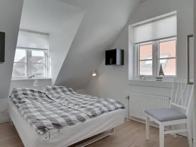 a white bedroom with a bed and a chair at Holiday Home Riki - 150m from the sea by Interhome in Blokhus