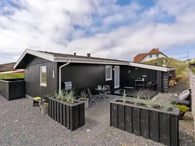 a black house with plants in front of it at Holiday Home Kiina - 100m from the sea by Interhome in Blokhus