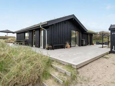 a black house on the beach with a wooden deck at Holiday Home Simeona - 140m from the sea by Interhome in Saltum