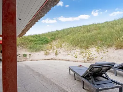 a chair and table on a patio next to a beach at Holiday Home Zora - 100m from the sea by Interhome in Harboør