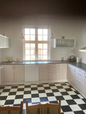 a kitchen with white cabinets and a checkered floor at Store Sand in Vemb