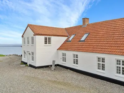 a white house with an orange roof next to the water at Holiday Home Thorge - 75m to the fjord by Interhome in Struer