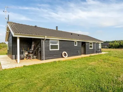 a black house with a wooden deck in a field at Holiday Home Sulki - 3-5km from the sea by Interhome in Frøstrup
