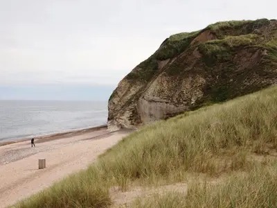 a person walking on a sandy beach next to the ocean at Apartment Rejhana - 500m to the fjord by Interhome in Øsløs
