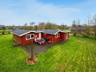 a red cabin with a deck in a field at Holiday Home Scarlet - 400m to the fjord by Interhome in Vinderup