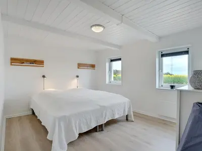 a white bedroom with a bed and two windows at Holiday Home Ailke - 2km to the fjord by Interhome in Thyholm