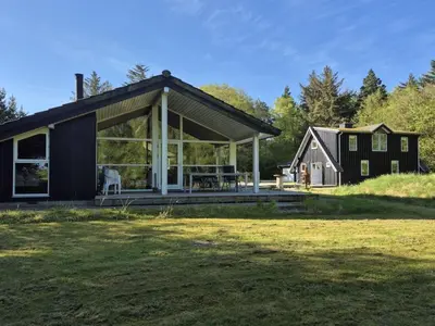 a black cabin with a deck and a house at Holiday Home Aswarth - 50m to the fjord by Interhome in Fur