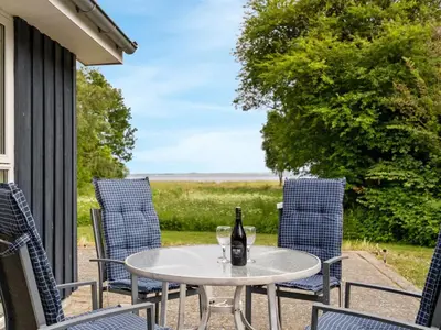 a table and chairs on a porch with a bottle of wine at Holiday Home Ødger - 150m to the fjord by Interhome in Åbybro