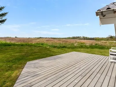 a wooden deck with a bench on a lawn at Holiday Home Eske - 200m to the fjord by Interhome in Åbybro