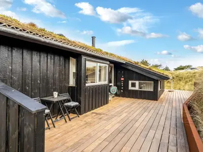 a black house with a wooden deck with a table at Holiday Home Nielsigne - 400m from the sea by Interhome in Blokhus