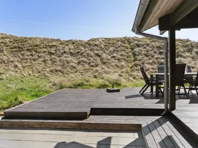 a patio with a table and chairs and a hill at Holiday Home Baltur - 650m from the sea by Interhome in Saltum