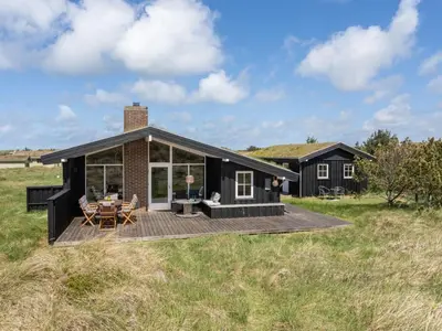 a black house with a deck in a field at Holiday Home Driss - 500m from the sea by Interhome in Pandrup
