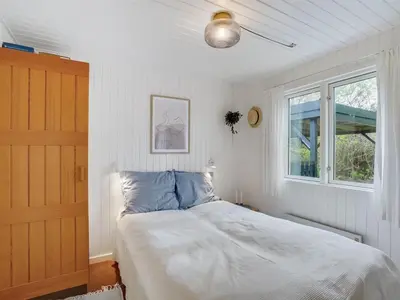 a white bedroom with a bed and a window at Holiday Home Thina - 750m to the fjord by Interhome in Løgsted