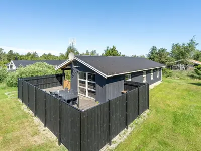 a black house with a black fence in a field at Holiday Home Ordan - 800m from the sea by Interhome in Fjerritslev