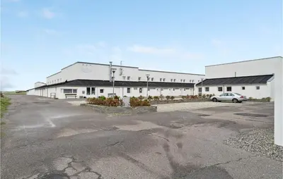 a large white building with a car parked in a parking lot at Gorgeous Apartment In Brovst With Wifi in Brovst