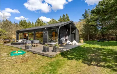a black cabin with a deck in the grass at 3 Bedroom Cozy Home In Blokhus in Blokhus