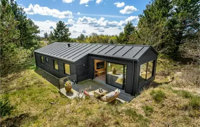 a black tiny house on top of a field at 3 Bedroom Cozy Home In Blokhus in Blokhus