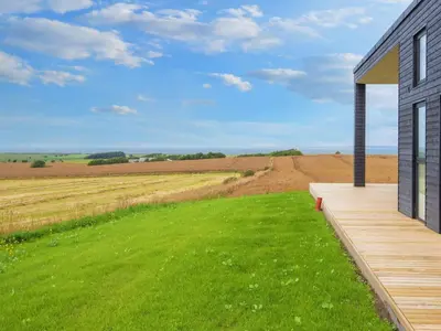 a house with a wooden deck next to a green field at 12 person holiday home in Lemvig-By Traum in Lemvig