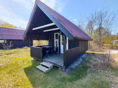 a small house with a deck with a table at Tranum Klit Camping og Hytteudlejning in Brovst